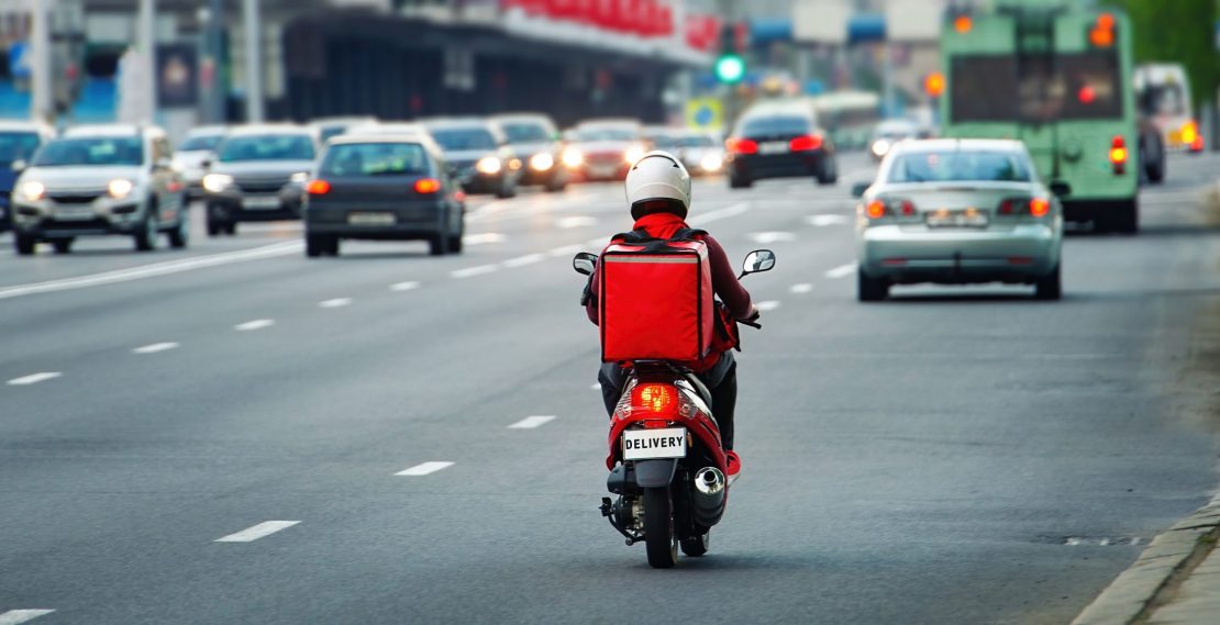 24 hours delivery service from cafes and restaurants. Takeaway, delivery boy on scooter with red isothermal backpack driving fast. Courier delivering food on motorbike to avoid evening traffic jams